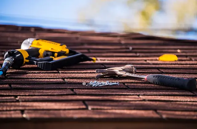 Close view of dark asphalt shingles with a cordless drill and hand tools resting on them